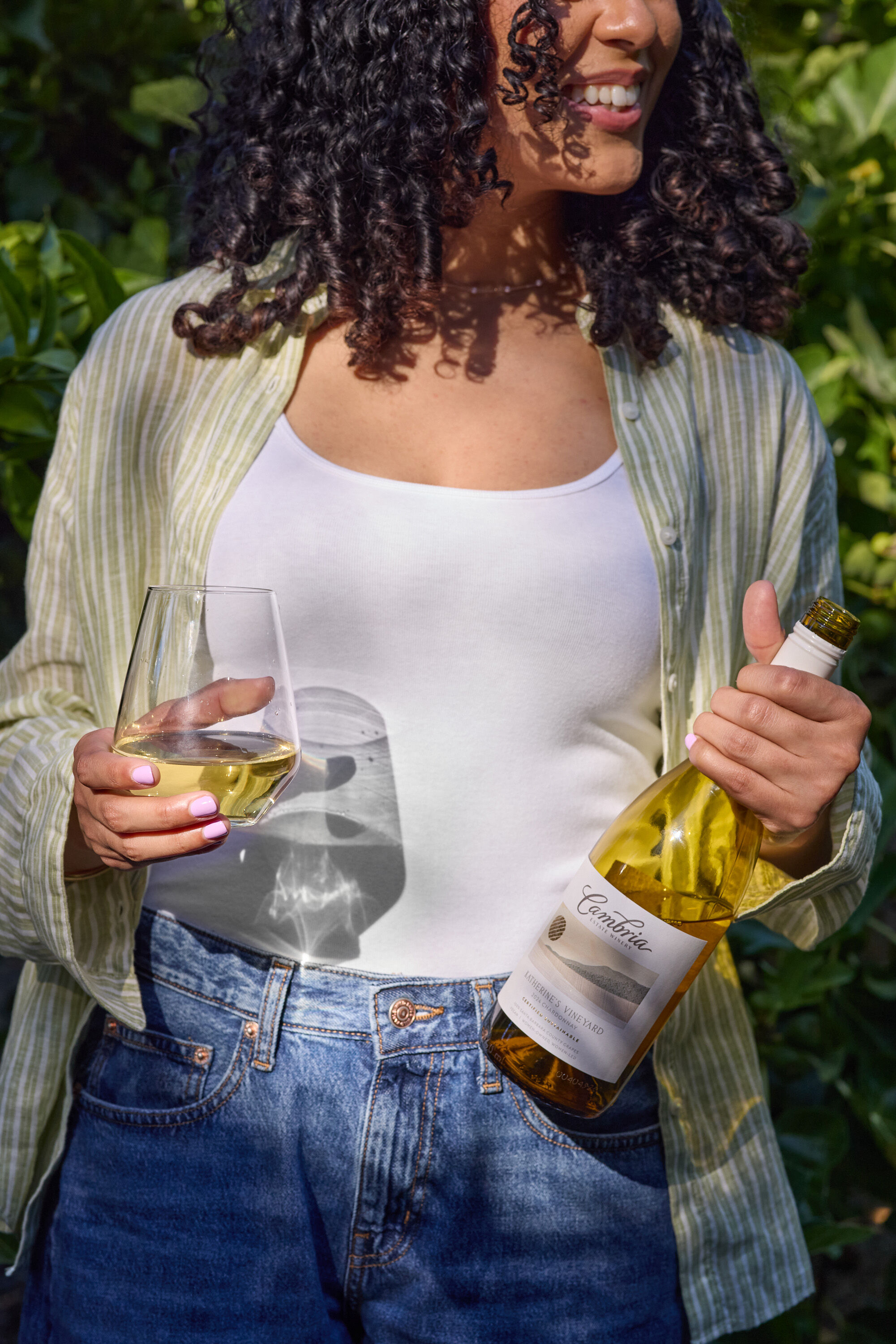 A glass of white wine on a black table outdoors with a person pouring wine into it